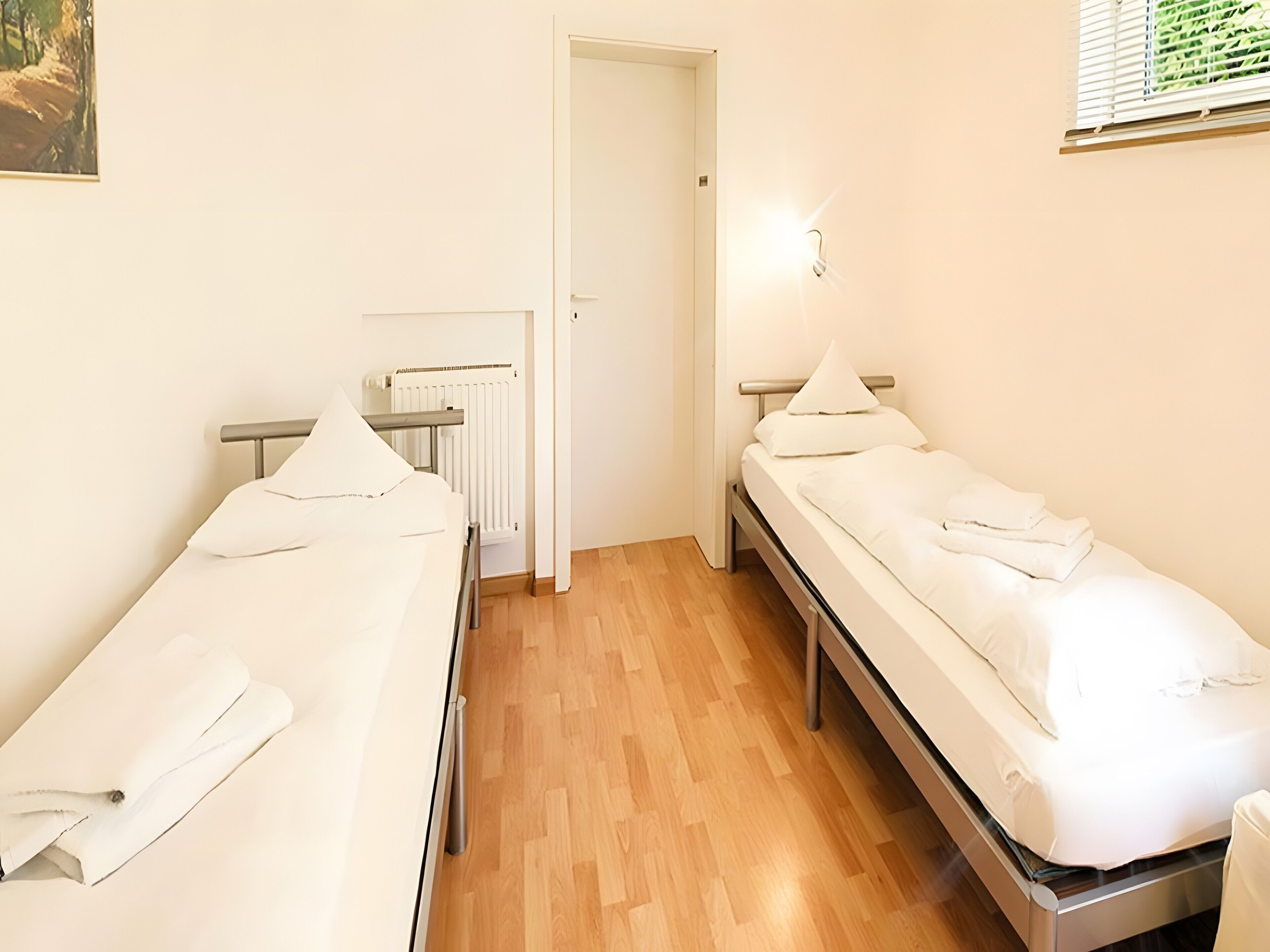 Una habitación de hotel con dos camas individuales, un radiador, una puerta y una lámpara.