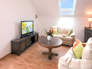 A living room with a television, a round coffee table, a sofa, and a window with a view.