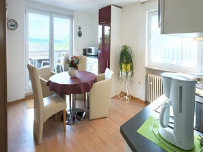 A dining area with a round table, chairs, a vase with flowers, a radiator, and a coffee maker.