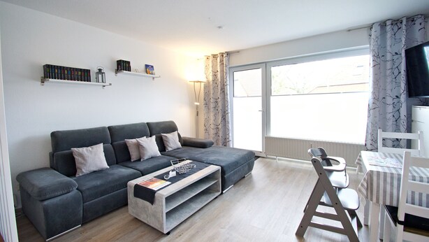 Ein modernes Wohnzimmer mit grauem Sofa, Couchtisch und Essbereich mit Tisch und Stühlen.