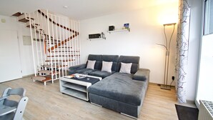 Ein modernes Wohnzimmer mit einem grauen Ecksofa, einer weißen Treppe und einem Bücherregal.