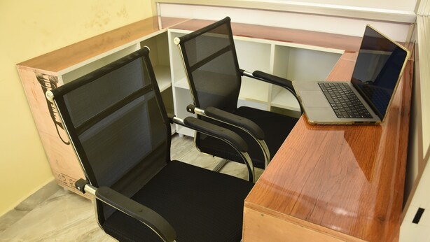 Un espacio de trabajo con dos sillas de oficina de malla negra, un escritorio de madera y una computadora portátil.