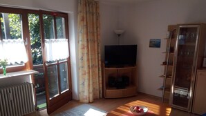 Olohuoneessa on televisio, puinen kaappi, sohva ja pöytä, jonka päällä on kulho täynnä hedelmiä.