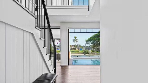 A modern interior with a wooden floor, a bench, a staircase, and a view of an outdoor swimming pool. - Luxury Villas Allambi Broadbeach (With Car Parking) (Broadbeach Waters)