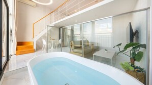 Un interior moderno con un balcón acristalado, una zona de estar con mesa y sillas, y una bañera grande.