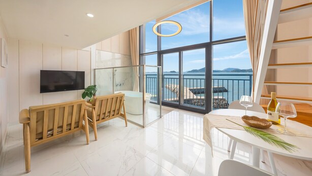 Habitación de hotel moderna con un balcón grande, una bañera, un televisor y un comedor con una mesa preparada para dos.