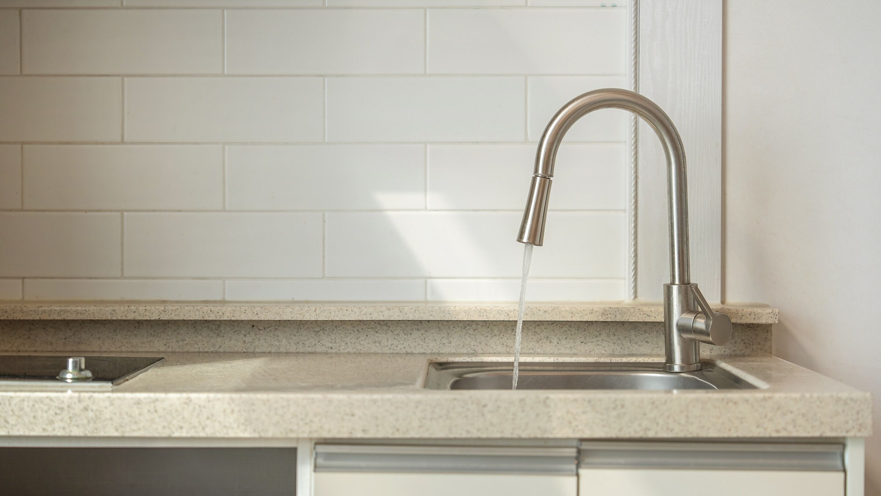 A kitchen with a stainless steel sink, a granite countertop, and white subway tiles on the backsplash.