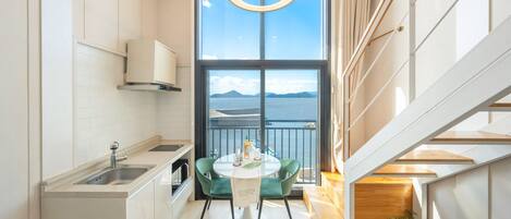 A modern kitchen with a view of the sea, a dining area with a table and chairs, and a staircase leading to an upper level.