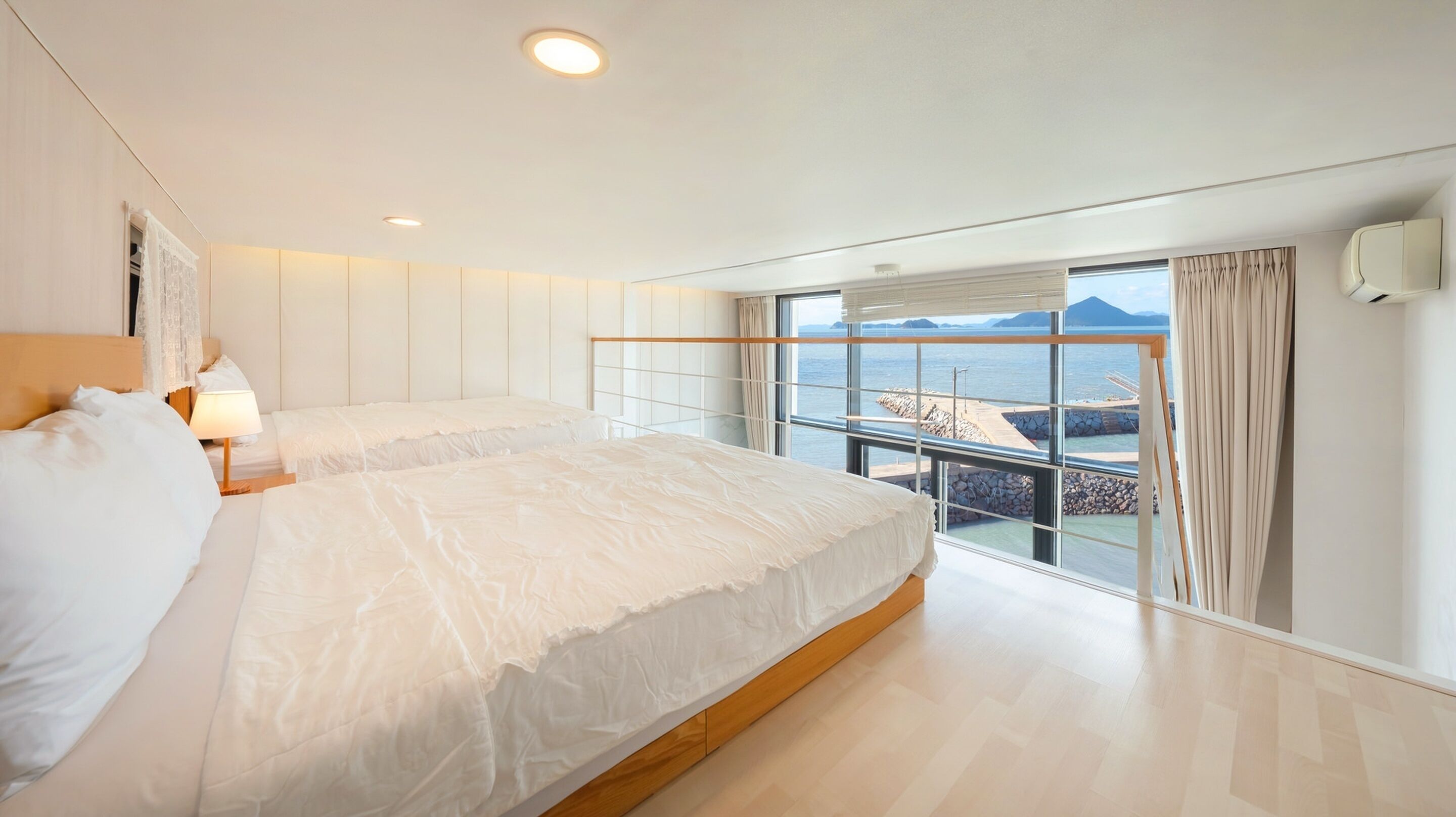 A hotel room with two beds, a large window with a view of the sea, and a balcony.
