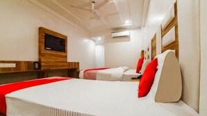 Una camera d'albergo con un letto grande, un letto più piccolo, una televisione fissata al muro e una ventola a soffitto.