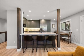 Cozinha moderna com ilha central, banquetas de bar e área de refeições com mesa e cadeiras.