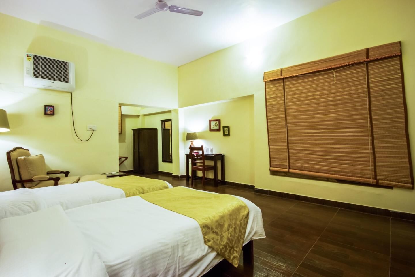 A hotel room with two beds, a desk, a chair, a ceiling fan, and a window with blinds.