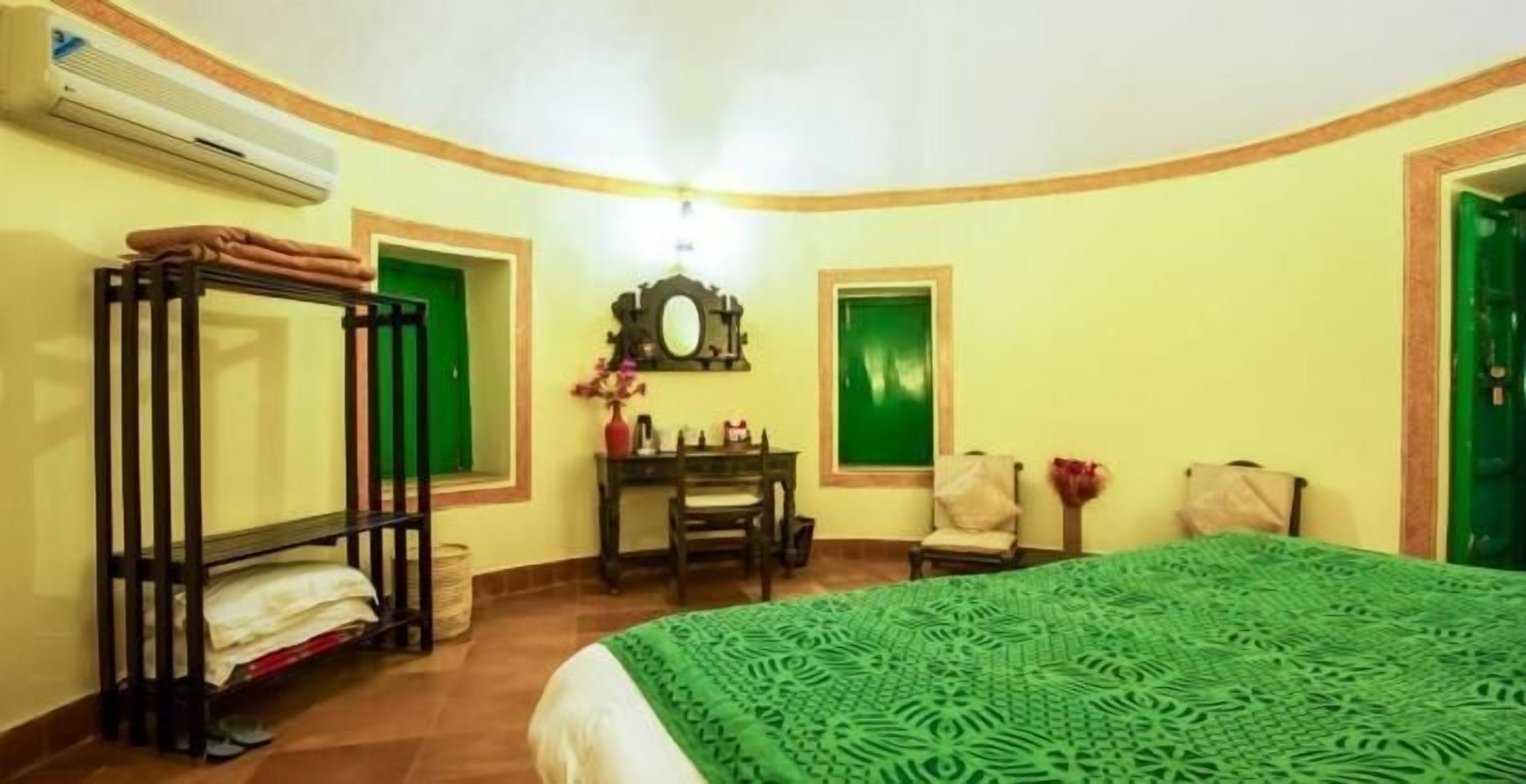 A room with a bunk bed, a desk with a chair, a small table with a vase, and a green door.