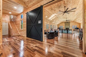 A spacious wooden interior with a large sliding door, a staircase, and a seating area with a view of the outdoors. - Indoor Pool + Game Rooms + Sports Court + Hot Tub + Golf Sim | Grand Timber (White Haven)
