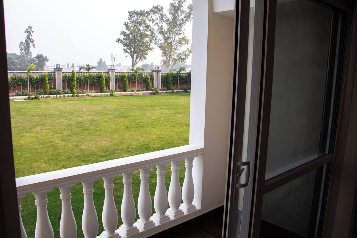 A view from a balcony with a white balustrade, overlooking a well-maintained lawn and a brick wall with greenery.
