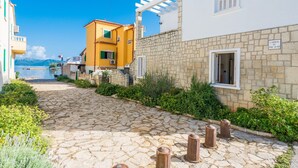 Um caminho de pedra pavimentada conduz a um edifício com parede de pedra e uma placa com a inscrição 'Carrer de Pure Quart'.