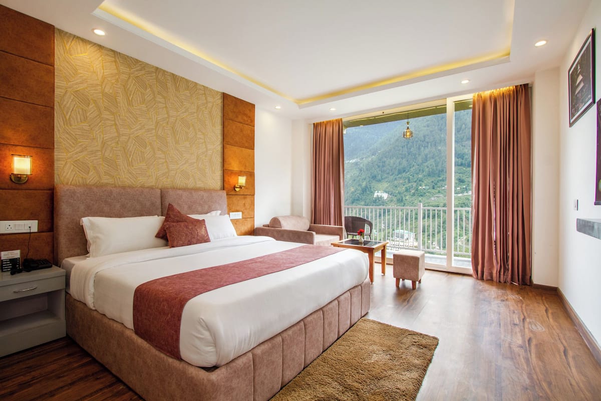 Un dormitorio espacioso con una cama grande, zona de estar y balcón con vistas a la montaña.