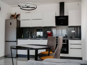 A modern kitchen with white cabinets, a black range hood, and a dining area with a table and chairs. - Modern Seget Vranjica Apartment With Terrace (Seget)