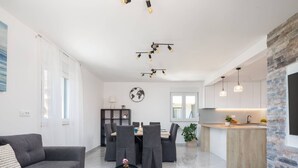 Ein modernes Wohnzimmer mit grauem Sofa, einem Essbereich mit Tisch und Stühlen sowie einer Küche mit Holzarbeitsplatte und Pendelleuchten.