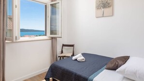 Ein Schlafzimmer mit Bett, Stuhl, Fenster mit Meerblick und einem Wandbild.