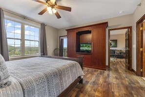 Ein Schlafzimmer mit einem großen Bett, einem Deckenventilator, einem Fernseher auf einer Holzkommode und Blick ins Freie durch ein Fenster.