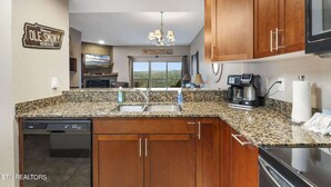 Una cocina moderna con encimeras de granito, armarios de madera, lavavajillas integrado y cafetera.