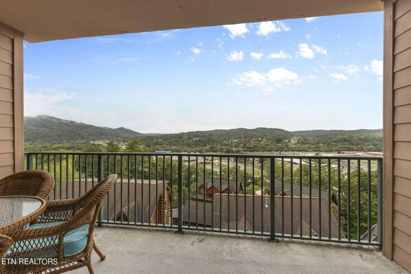 Ein Balkon mit Korbmöbeln, Blick auf einen Parkplatz und entfernte Berge.