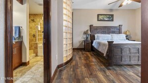 Un dormitorio con una cama de madera, una mesita de noche, un ventilador de techo y un baño con ducha y barra para toallas.