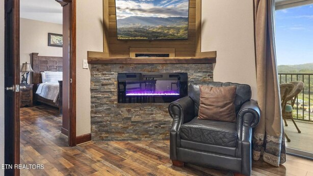 Una sala de estar con chimenea de piedra, televisor montado, sofá de cuero y balcón con vistas al campo.