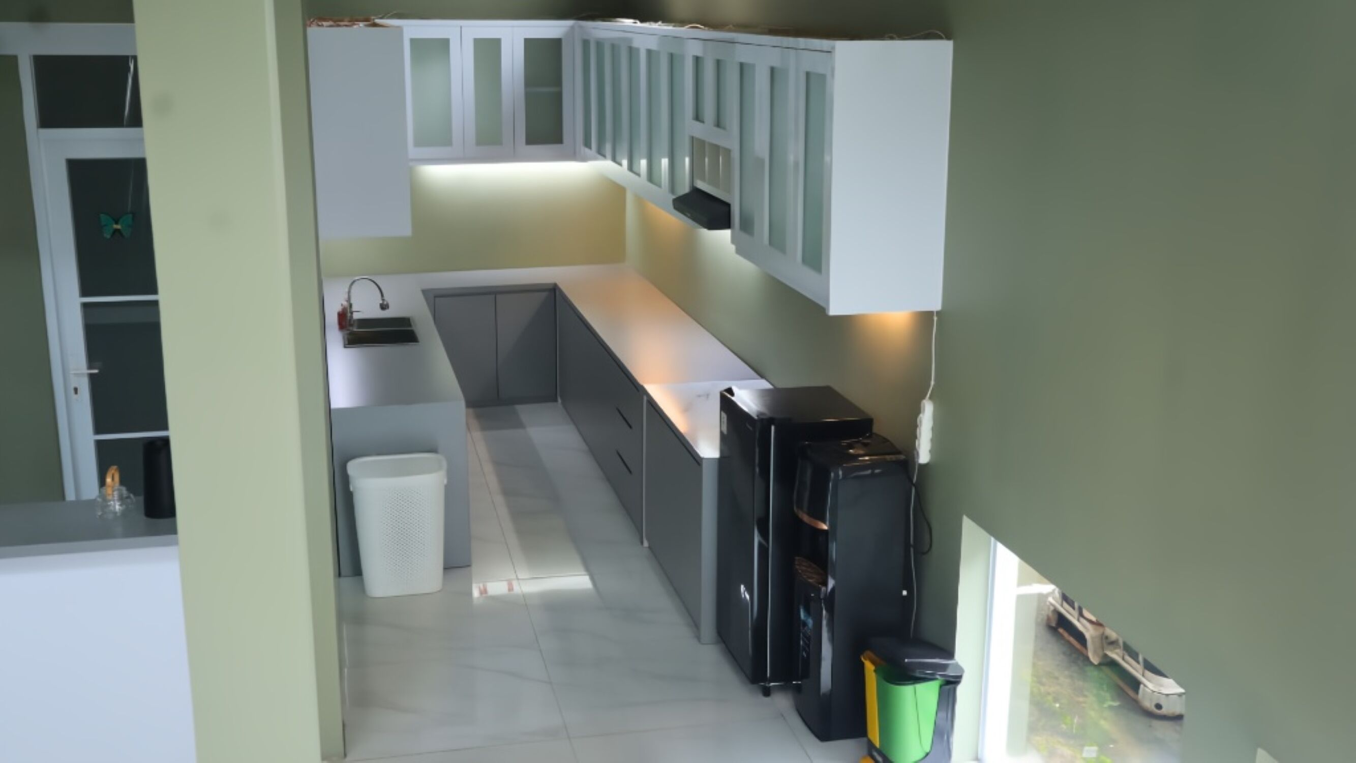 Eine kompakte Küche mit weißen Schr änken, einem schwarzen Kühlschrank und einer kleinen Mülltonne.