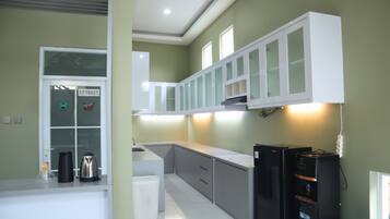 A modern kitchen with white cabinets, a stainless steel kettle, and a black refrigerator.
