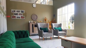 A modern living room with a green sectional sofa, two grey armchairs with green cushions, a wooden coffee table, a marble-patterned rug, a clock, and a window with a view of greenery. - DeBali Villa Countryside by Simply Homy (Banyuresmi)