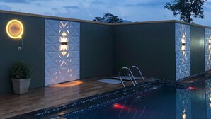 A modern outdoor pool area with a wooden deck, a glass barrier, and decorative wall lighting. - DeBali Villa Countryside by Simply Homy (Banyuresmi)