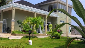A two-story house with a covered patio, a lawn, and various plants. - DeBali Villa Countryside by Simply Homy (Banyuresmi)
