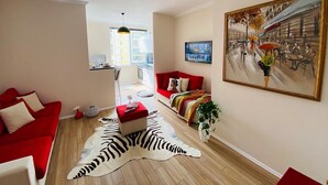 A living room with a red sofa, a zebra print rug, a painting, and a kitchen in the background. - SUNLIT ERISI’s HOUSE - City center (Tiranë)
