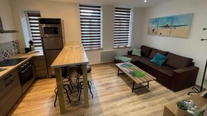 Un espacio habitable compacto con kitchenette, una mesa de comedor, un sofá y un cuadro en la pared.
