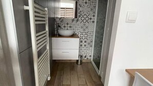 Un baño estrecho con un lavamanos blanco, un espejo encima y un salpicadero de azulejos estampados.