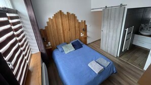 Un dormitorio moderno con cabecera de madera, edredón azul y una mesita de noche con lámpara.