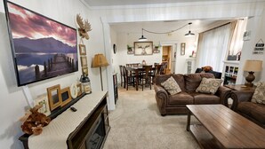 Una sala de estar acogedora con chimenea, un televisor montado en la pared y una zona de comedor con mesa y sillas.