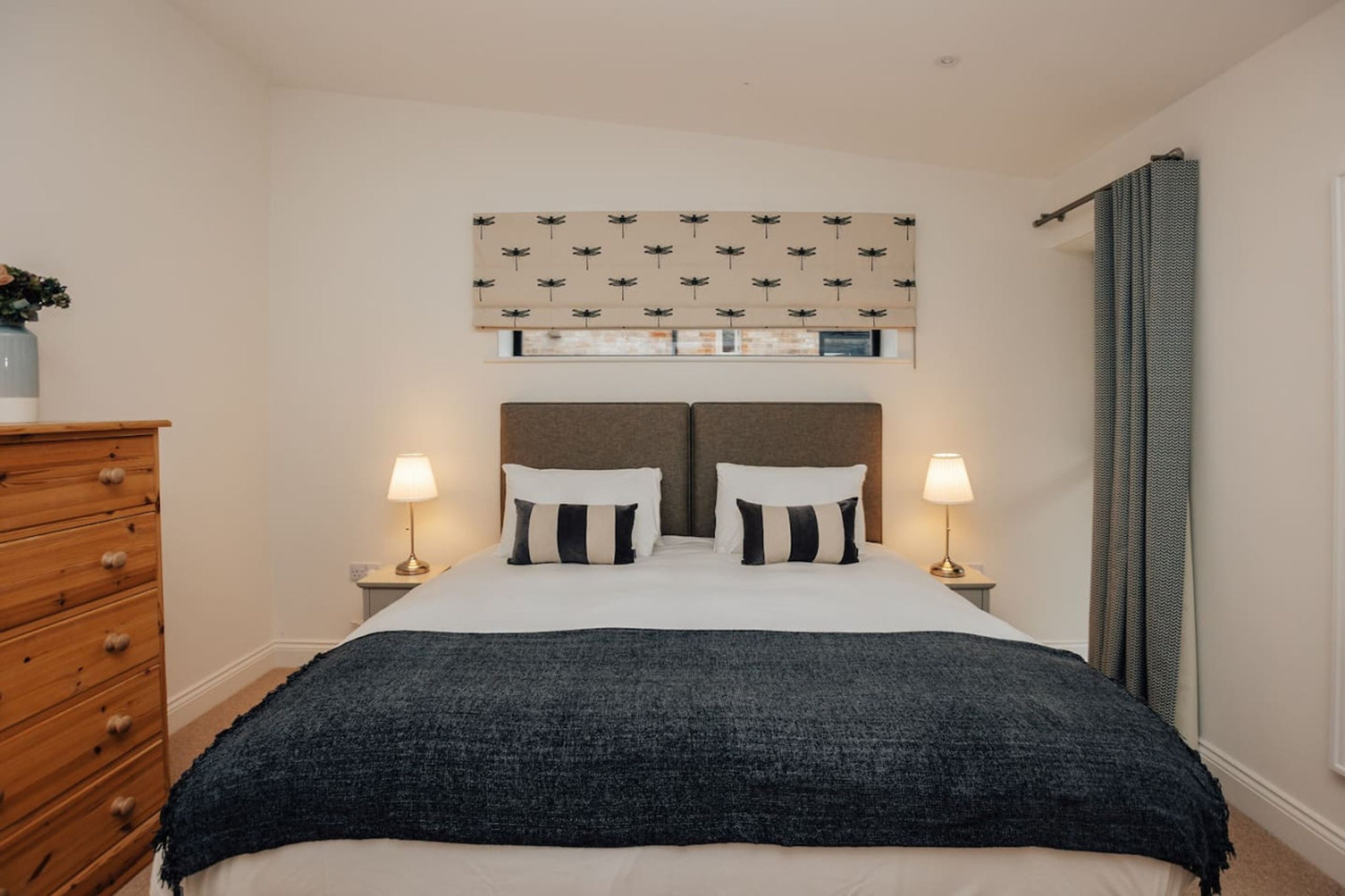 Una camera da letto con un letto, due comodini con lampade, un settimino in legno e una finestra con tende.