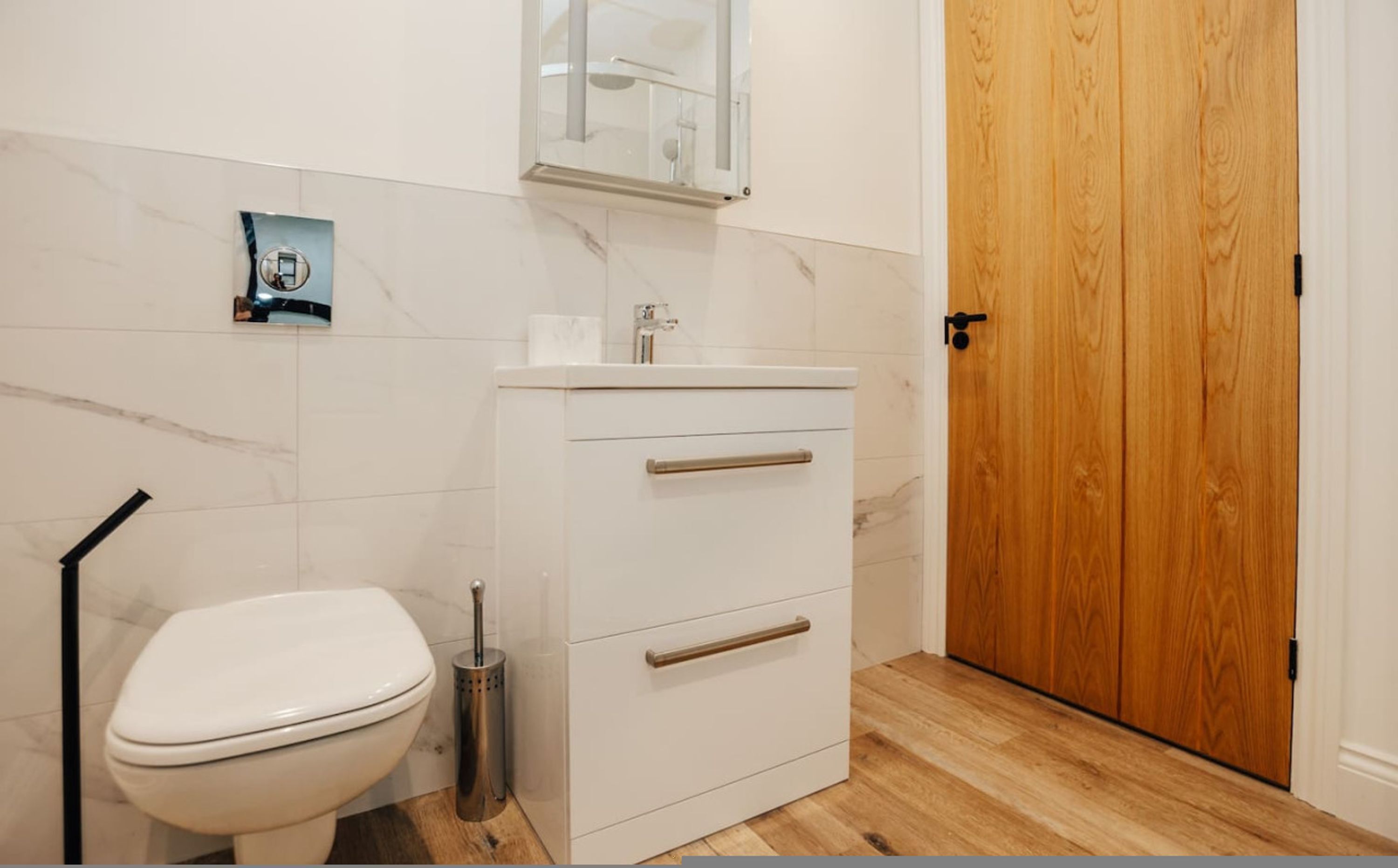 A bathroom with a toilet, a sink with a mirror above it, and a wooden door.