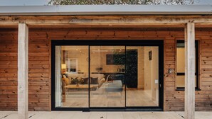 A modern building with a wooden facade and large glass doors leading to an interior with a living area and kitchen. - Cart Shed 2 - From 140 Per Night (Oxford)