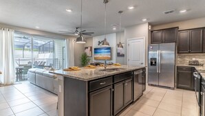 A modern kitchen with a large island, stainless steel appliances, and pendant lighting.