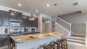 A modern kitchen with dark cabinets, stainless steel appliances, granite countertops, and wooden bar stools.