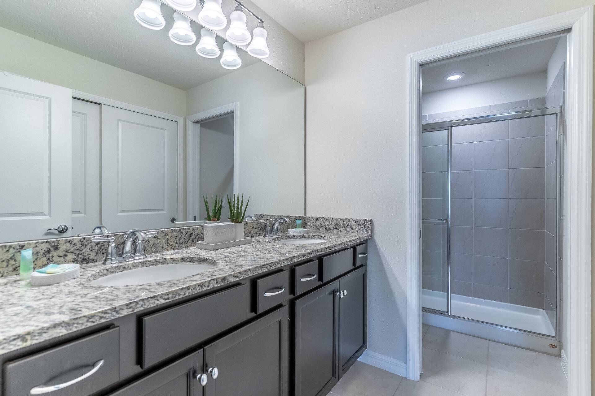 A bathroom with a double sink vanity, dark cabinets, a shower with a glass door, and a ceiling light fixture.