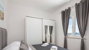 A bedroom with a bed, pillows, a window with curtains, a mirror, and a view of the city.