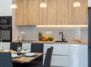A modern kitchen with wooden cabinets, a built-in microwave, and a dining area with a table set for two. - Contemporary Apartment With Terrace and Spacious Garden (Kastela)