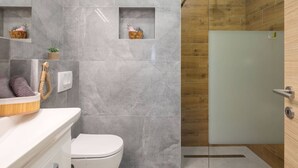 A modern bathroom with a toilet, a shower with a glass door, and a vanity with a mirror and a basket of toiletries.