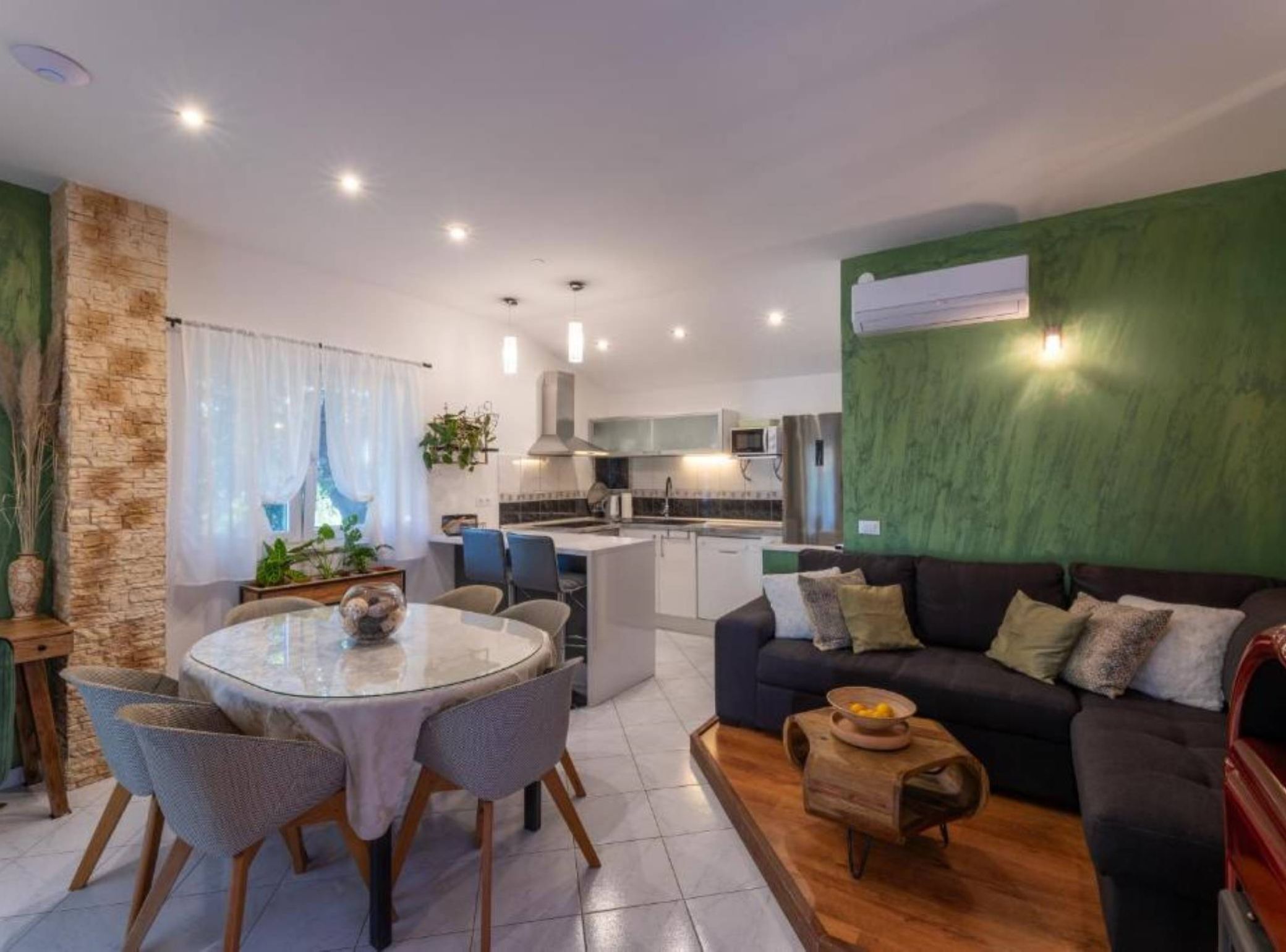 A modern living room with a round glass table, two chairs, a dark sofa with cushions, and a small wooden coffee table.