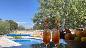 Vista de la piscina con dos bebidas, un cuenco de fruta y un tobogán.